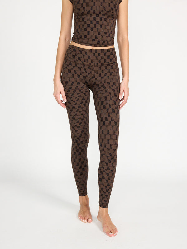 Eine Frau steht barfuß vor einem schlichten Hintergrund und trägt by malene birger Polene - Leggings mit Brand-Details und ein passendes Crop-Top mit schwarzem geometrischen Muster. Ihre Arme liegen entspannt an den Seiten, und das Bild ist an den Schultern abgeschnitten.