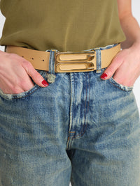 Eine Person, die eine blaue Jeans mit hoher Taille, ein olivgrünes, geripptes Oberteil und den Victoria Beckham Jumbo Frame - Ledergürtel mit goldfarbener Schließe trägt, hat die Hände in den Taschen ihrer Jeans.